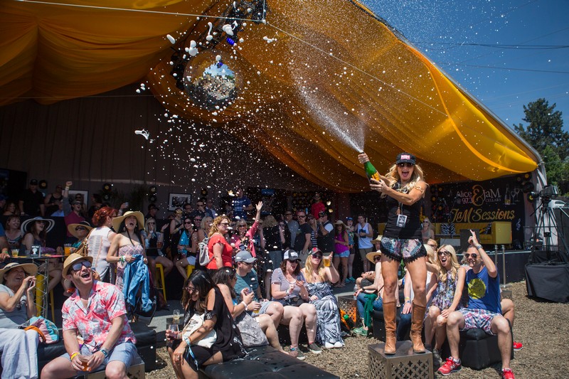 Woman popping cork of JaM Cellars wine in front of outdoor crowd with tent in background