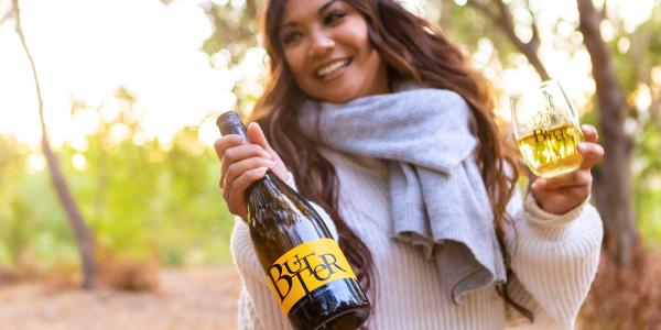 Woman with cozy scarf holding a bottle and glass of JaM Cellars Butter