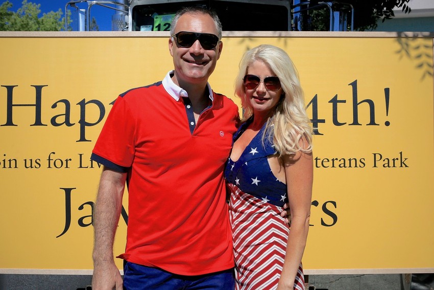 Man in red shirt and woman in red, white and blue outfit  in front of Happy 4th sign