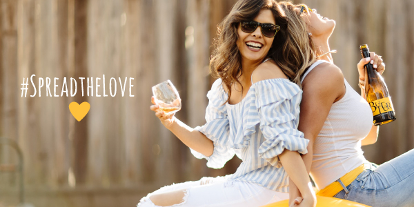 Two women sitting back-to-back with text #SpreadtheLove and holding Butter Chardonnay